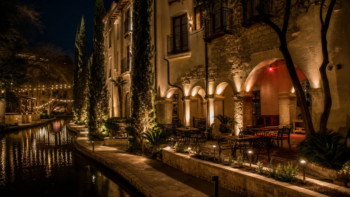 San Antonio riverside hotel and restaurant exterior at night with warm LED facade, pathway and landscape lighting reflecting on the water